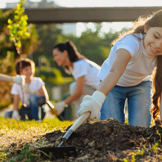 A group of children and adults wearing white shirts and gloves joyfully participate in a community tree-planting activity, fostering environmental awareness and teamwork.