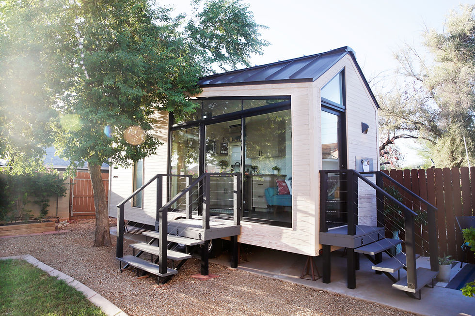A tiny house with large glass windows, sits in the backyard surrounded by a wooden fence a