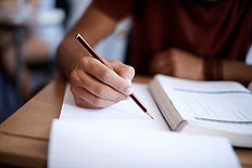 A person writes with a pencil in an open notebook on a desk