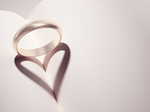 A ring placed on an open book casts a heart-shaped shadow, symbolizing love and commitment.