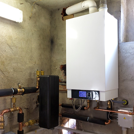 A white condensing gas boiler with exposed pipes and a control panel, in a utility room