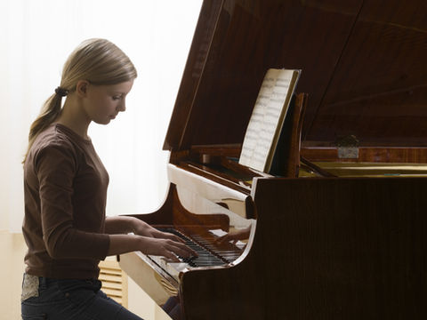 Jeune fille jouant du piano droit avec partition, dans une pièce lumineuse; ambiance calme et concentrée.
