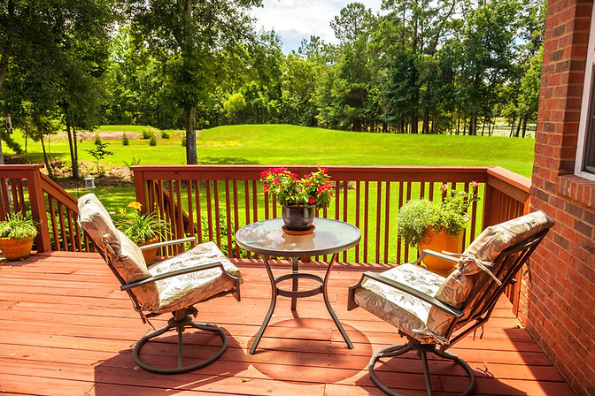 Close-up of a cozy wooden deck patio setting with small table, potted flowers, and garden views