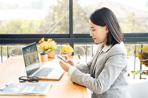 A woman looking at a cellphone with a laptop on the table