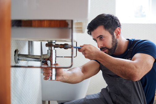 Plumber fixing pipes under a sink with a wrench For Facilities Ltd