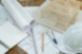 Blueprints and architectural tools with rolled plans spread on a table with a small wooden house model