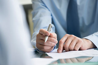 a person in a blue shirt holding a pen, gesturing to papers on a desk