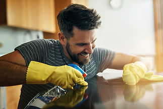 Man wearing yellow protective gloves wiping polished wooden table