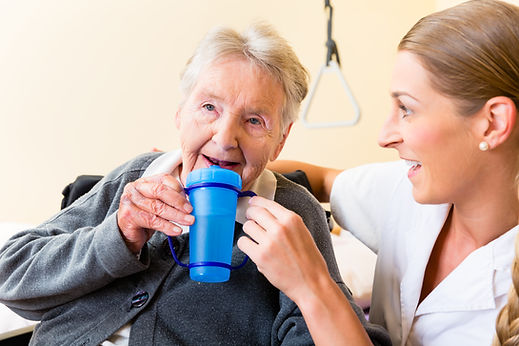 Nurse in nursing home giving drink to elderly woman sitting in wheelchair