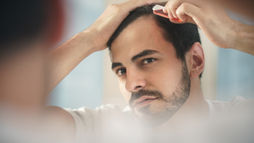 Man trims his hairline in a mirror with a razor, concentrating in a softly lit bathroom.