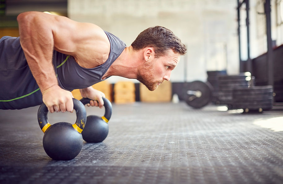 A man in a gym performs push-ups using kettlebells on a rubber floor