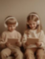 Two kids wearing headphones, smiling and using tablets. They're seated indoors with a beige background, dressed in matching light outfits.