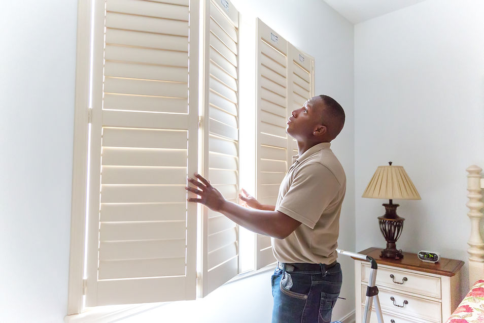 A man opening traditional white solid panel wooden bedroom shutters to let light into a nursery room