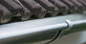 Close up view along a dark metal gutter system fixed to a tiled house roof line filled with moss and debris