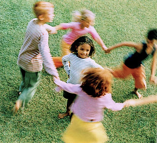 Children engaged in outdoor circle game on natural playground surface, building social skills through group play