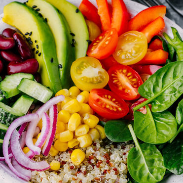Colourful salad bowl with spinach, tomatoes, corn, avocado, beans, and quinoa. Fresh ingredients arranged in a white dish on a grey table.