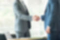 Two men in suits shaking hands over a desk