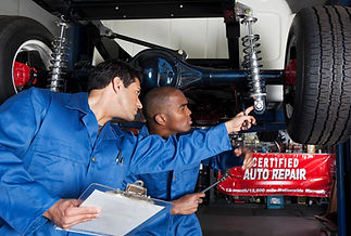 Two mechanics inspecting the rear suspension and axle of a car on a lift