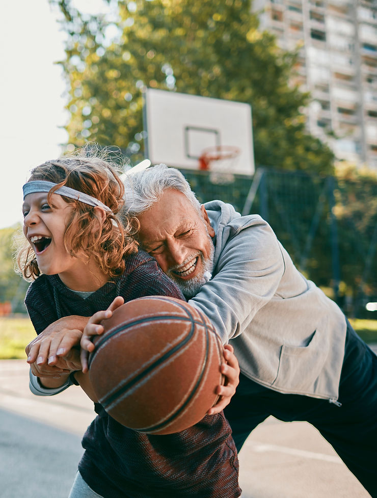 A joyful moment of an elderly man and a young child playing basketball together on an outdoor court, laughing and enjoying the game. This image represents Episode 80: How Play Leads to Increased Wellness, highlighting the benefits of play for mental, physical, and emotional well-being at any age.