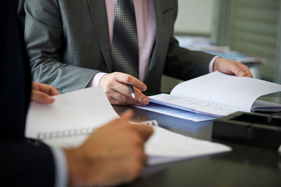 Two professionals in business suits reviewing paper documents at a conference table.