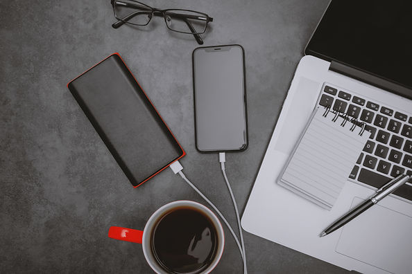 Top-view of a laptop, mobile phone charging with power bank and coffee mug on work desk