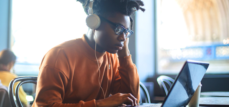 A student sitting at a desk with a laptop open, focused on studying. The student is wearing headphones and appears to be deep in concentration. The background is blurred, emphasising the student and their study materials.