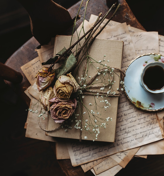 Aging letters and a journal arranged with dried roses on top and a cup of tea to the side.
