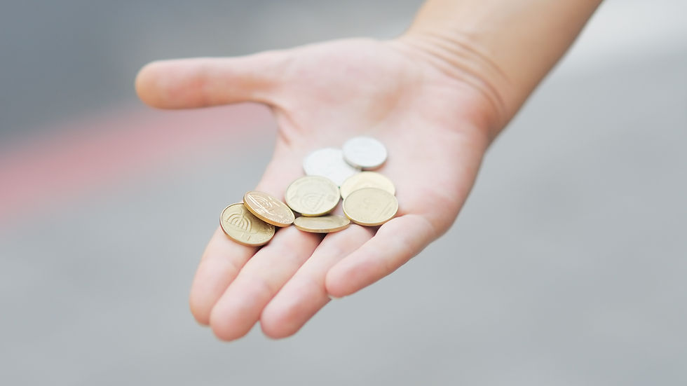 A hand holding several gold and silver coins against a blurred gray background, creating a sense of simplicity and focus on the coins.
