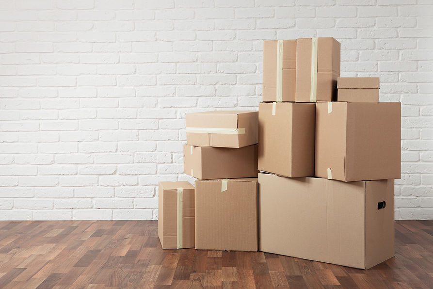 Stacked cardboard boxes on a wooden floor against a white brick wall
