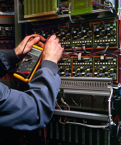 A technician uses a multimeter to test the voltage in an electrical panel with numerous wires