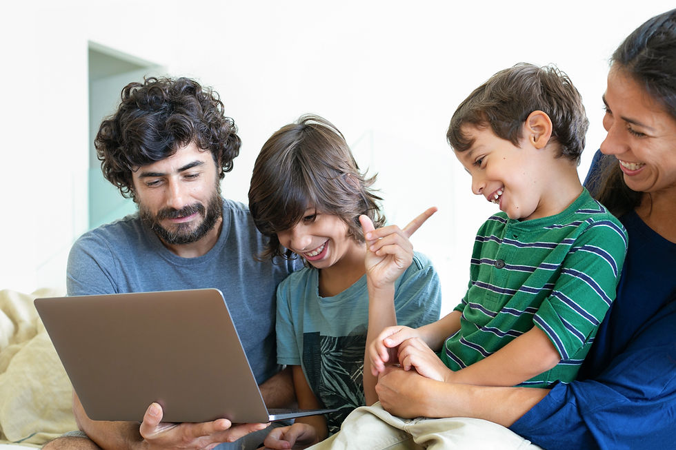 Family of four smiling and gathered around a laptop at home.
