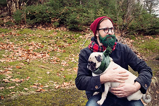 Man holding a pug dog wrapped in a scarf outdoors
