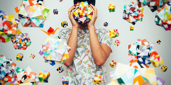 Man surrounded by many origami shapes, illustrating the creative strengths and organisational differences often seen in neurodivergent adults. Used to represent neurodiversity-affirming assessment services.