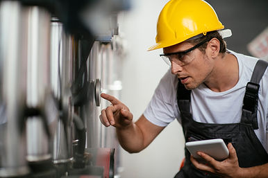 A man wearing a yellow hard hat and safety glasses inspects industrial equipment