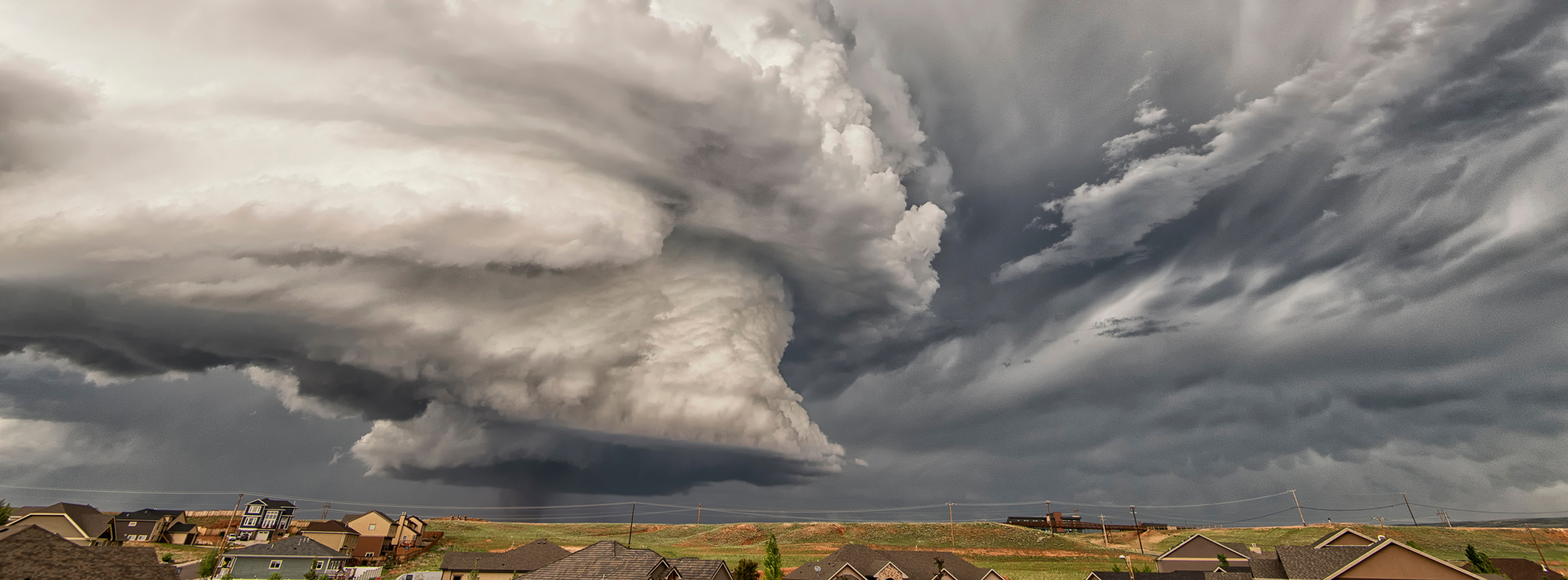 Stress im Alltag der Natur: Gewitterwolken türmen sich über einer Vorstadtsiedlung; dunkler Himmel, Häuser und Stromleitungen unten.