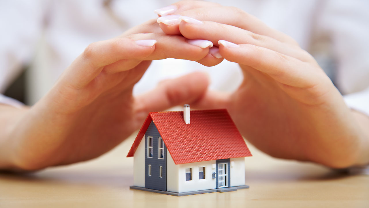 Female hands saving small house with a roof