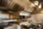 Interior view of restaurant kitchen, pots on stovetop, grill and extractor hood