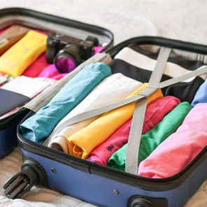 Open suitcase filled with colorful clothes, a passport, camera, sunblock, and a tablet, ready for holiday travel