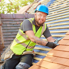 A roofer nails on the roof tiles with worker in a blue hat and green vest
