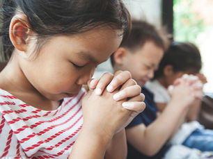 Children praying with their heads bowed, eyes closed and hands folded.