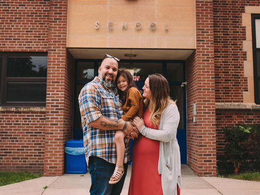young family smiling in front of school building