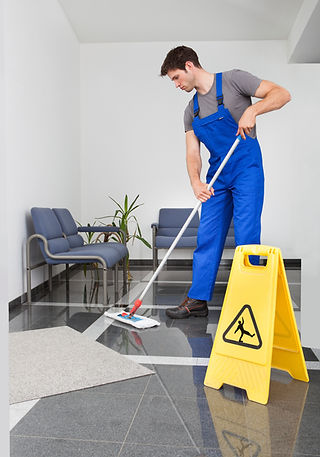 Person mopping a shiny office floor with gray tiles, near a yellow caution sign.