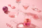 Assorted pink drinks in elegant glasses on a pink background with ribbons, a glittery purple ball, and a glass sphere. Festive mood.