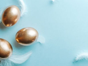 Three gold eggs with white feathers on a light blue background. The scene is minimalist and serene.