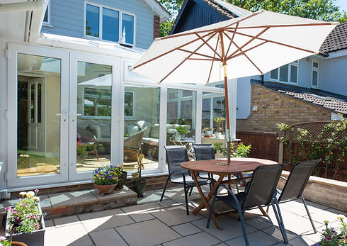 A general view of a slabbed patio, with wooden table and black chairs furniture with paras