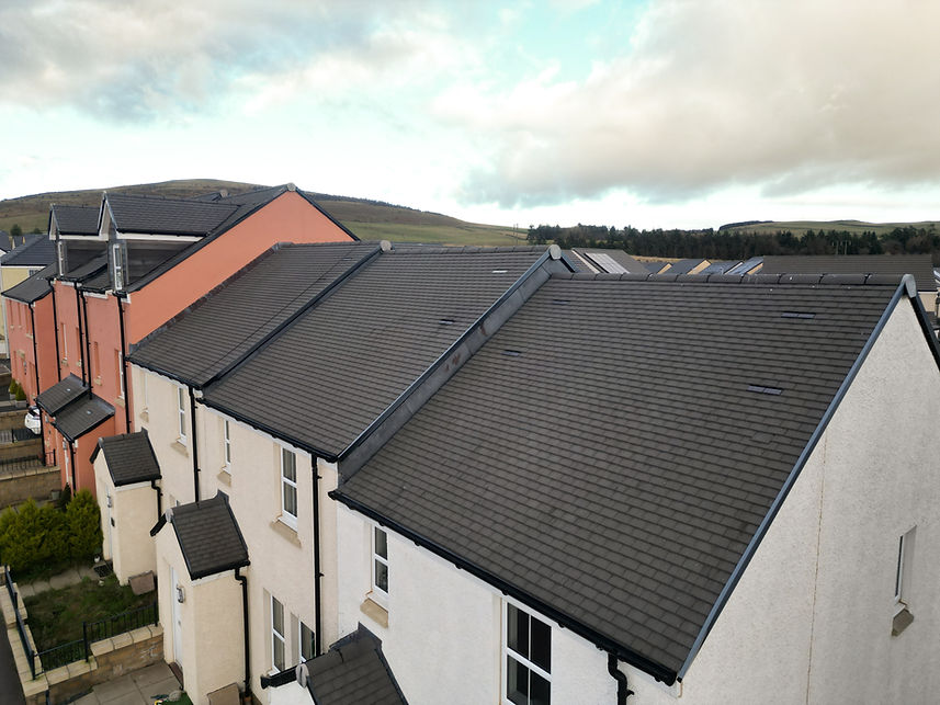 Aerial view of residential buildings with sloped roofs, featuring a mix of colors including white and pink.