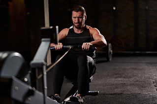 A man intensely works out on a rowing machine in a dimly lit gym.