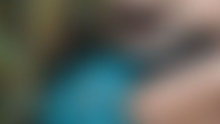 Woman in a red swimsuit floats in a blue-tiled pool surrounded by lush greenery and tropical huts with thatched roofs. Relaxed mood.