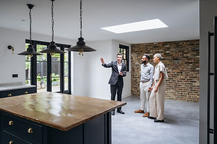Male estate agent showing a spacious, modern open plan kitchen and dining area to a couple