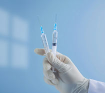 A doctors hand holding two needles for a vaccine shot